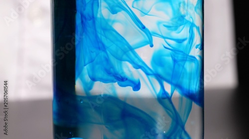 Schilderij op canvas Vibrant Blue Dye Swirling and Dispersing Inside a Clear Glass Water Container