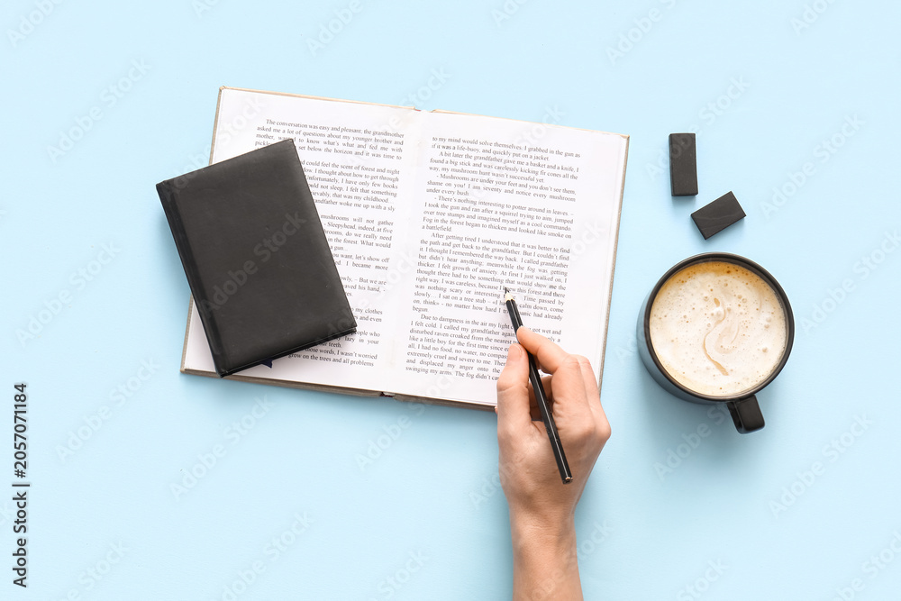 Fototapeta premium Female hand with pencil, open book and cup of hot coffee on blue background
