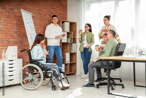 Female business speaker in wheelchair with people during seminar at office