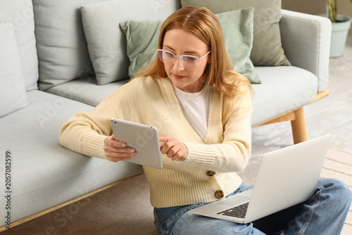 Focused woman in glasses using digital tablet and laptop for remote work or o...