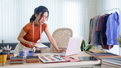Asian fashion designer working with laptop and fabric samples in home studio