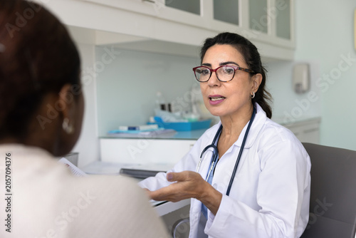 Obraz na płótnie Serious mature general practitioner woman in lab coat and glasses talking to you