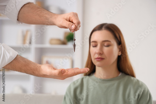 Male psychologists hands with pendulum hypnotizing woman in office, closeup
