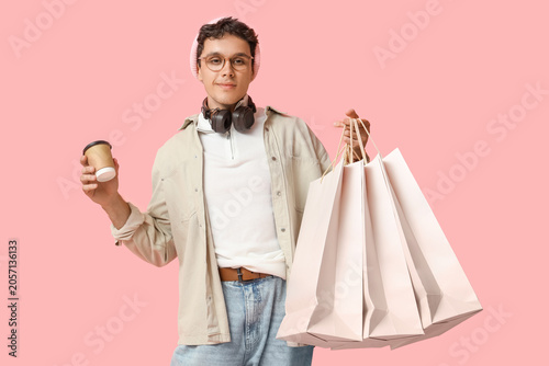 Stylish young man with shopping bags and coffee on pink background