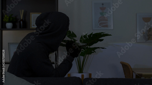 Billede på lærred Masked Intruder in Dark Hoodie Sitting in Dimly Lit Living Room