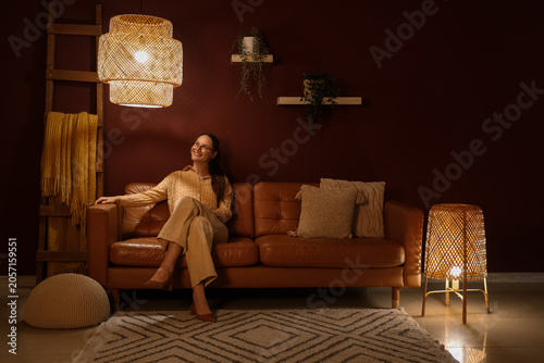 Smiling woman relaxing on brown leather sofa in cozy living room with woven l...