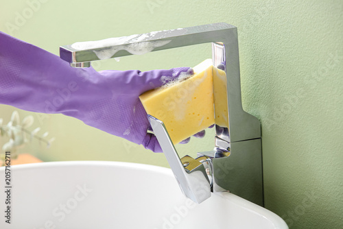 фотографія Hand in purple rubber glove cleaning chrome faucet with yellow sponge and soapy