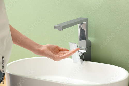 Foto Modern chrome faucet and white ceramic sink with persons hand reaching for water