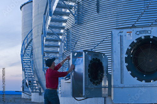Quadro su tela a man turns on an aeration fan on a  grain storage bins in the evening