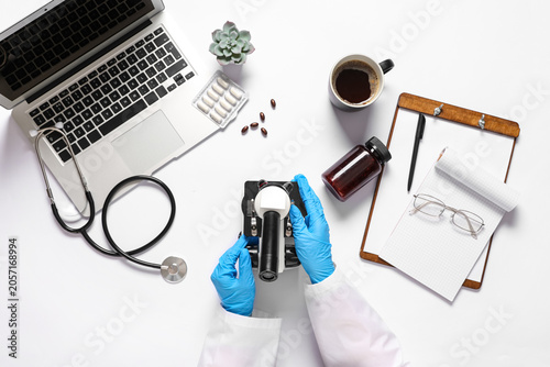 Hands of female scientist with modern microscope, cup of coffee, pills and la...