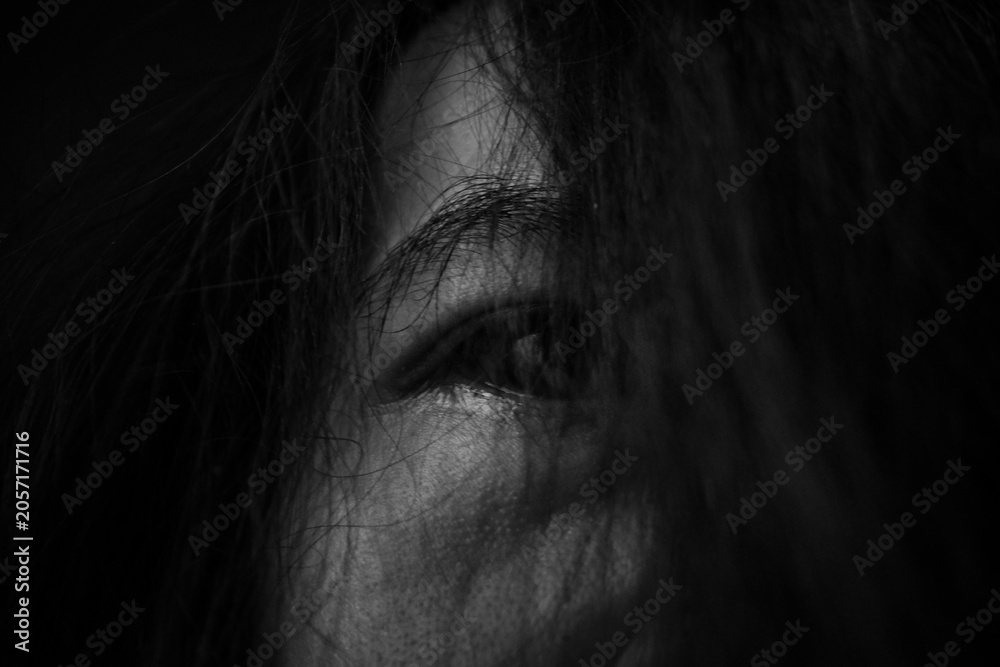 Fototapeta premium Close Up of Eye Hidden Behind Hair in Darkness Showing Fear and Anxiety