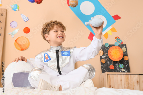 Bilde på lerret Smiling young boy in astronaut costume playing with toy rocket, space exploratio