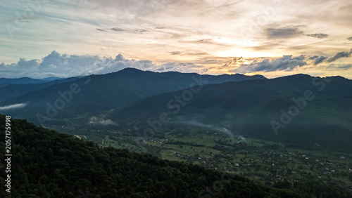 Tableau sur toile Soft sunset light spreads over a mountain valley where specks of smoke and fog linger above fields