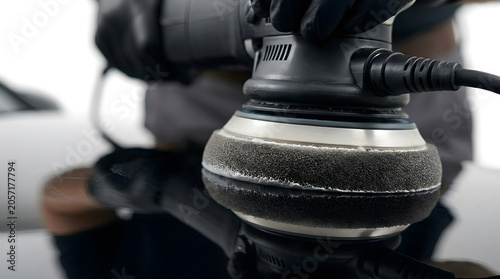 Close-up of professional paint correction specialist using a dual-action orbital polisher on a black car hood to remove scratches