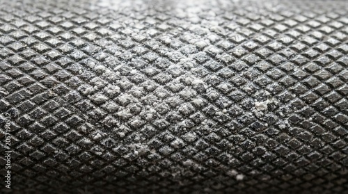 Close-up macro shot of a knurled metal barbell grip with white chalk residue