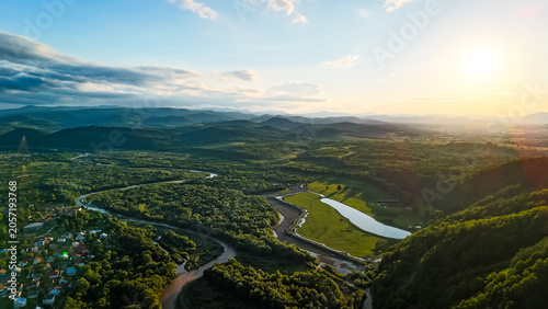 Aerial view of a vast valley at sunset with rivers, lake shining and clusters of trees