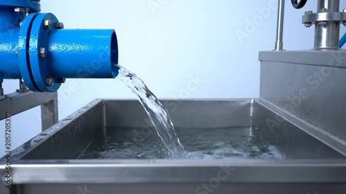 Industrial water flowing from blue pipe into stainless steel tank.