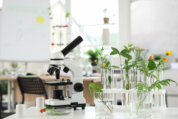 Modern microscope and test tubes with plants on shelf in Biology classroom, closeup