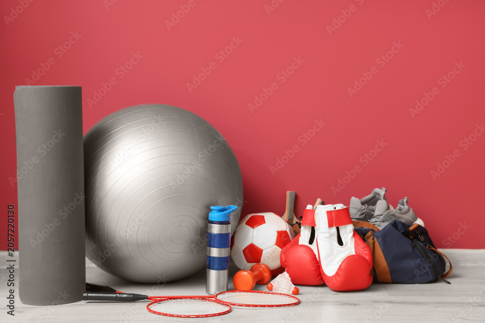 Naklejka premium Different sports equipment and bag with shoes on floor near red wall