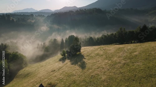 Dynamic timelapse of rapidly moving morning mist in a rural mountain valley with striking sunbeams through trees, scenic golden hour in the Bran hills, Carpathians, static aerial view