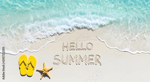 Text hello summer written on a sandy beach. Tropical holiday concept. Yellow flipflops and a starfish resting near gentle ocean waves.