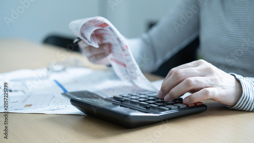 Close up of hand using a calculator while checking receipts and invoices for monthly bills  household budget and debt calculation.
