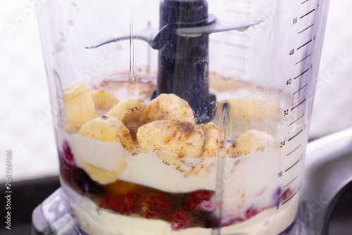 Making healthy berry banana smoothie in a blender container. Close up of blender filling with milk, banana and red berries. Fresh fruit smoothie ingredients with yogurt and cinnamon in blender. 