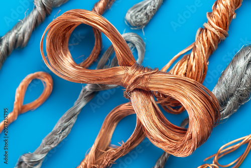Copper wire loop on blue background with copper and silver cables.Close up of metal wires, raw copper and silver industrial cable. Bundles of bright copper wire and silver metal strands on blue.