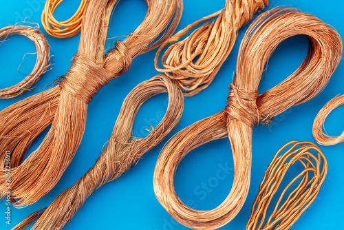 High quality scrap copper wire bundles on blue background. Raw metal material for recycling and industry. Electrical copper cable sorting.Industrial copper wire coils for recycling process.