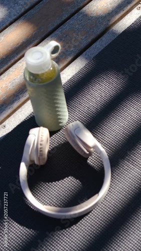 Vertical video: Tilting handheld camera revealing bottle and beige headset details on bench
