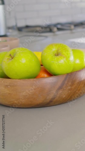 Vertical video: Panning camera revealing wooden fruit bowl on countertop with apples bananas knife