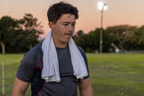 White towel is resting over dark athletic shirt on grassy sports field at dusk, floodlights glowing