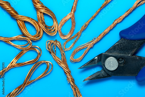 Copper wire loops with wire cutter pliers on blue background. Stripped copper wires and diagonal cutting pliers for electrical work. Macro shot of recycling copper wire and metal cutter tool.