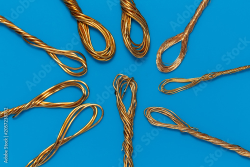 Copper wire loops on a blue background. Bundles of bright copper wires arranged on blue surface. Close-up of twisted golden copper wire recycling concept.