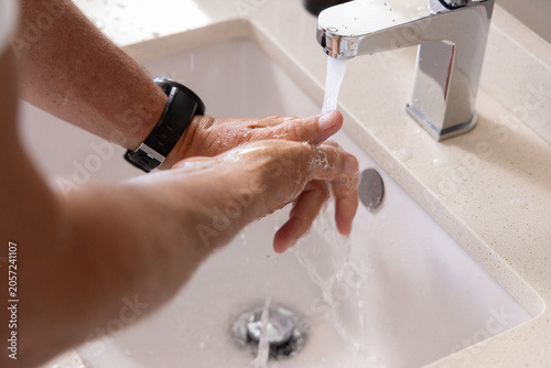Fotografie Man rinsing hands under chrome faucet at bathroom sink, wearing black wristwatch