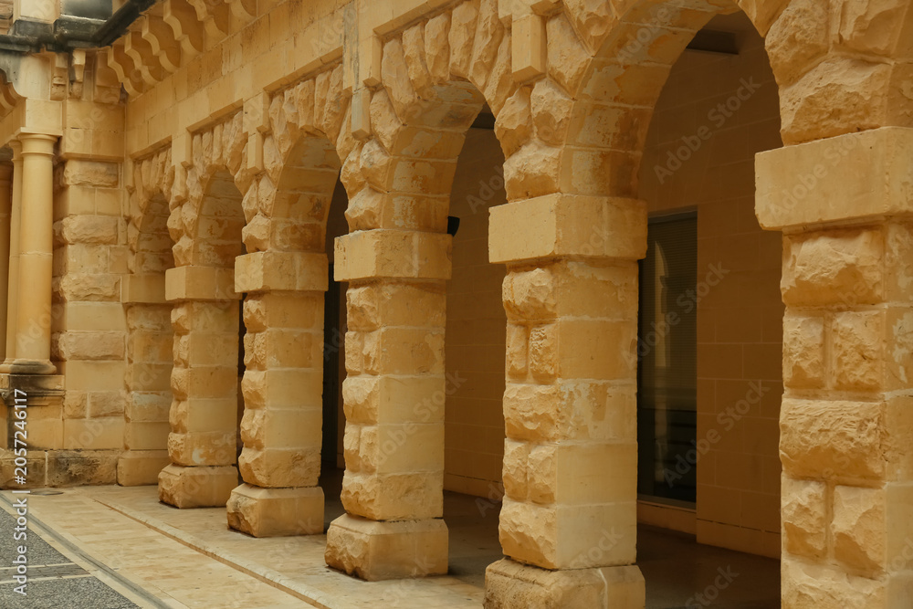 Naklejka premium Historic stone archway corridor with textured columns and arches, architectural detail and ancient building design, the facade features rough-hewn masonry in yellow and beige tones