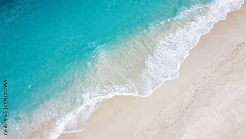 Aerial birdseye view of remote exotic tropical island with white frothy waves, sandy beach, and turquoise ocean water in paradise