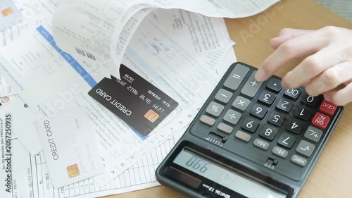 Hand pressing a calculator while reviewing monthly bills, receipts and credit card expenses for household budget planning and debt management.