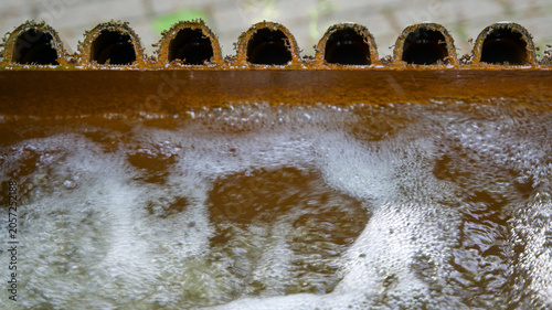 Foto Muddy water bubbling inside a rusty metal industrial filtration or settling tank with a row of overflow pipes, close-up