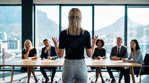 Photos Rear view of a confident businesswoman presenting to a diverse team in a spacious modern board room