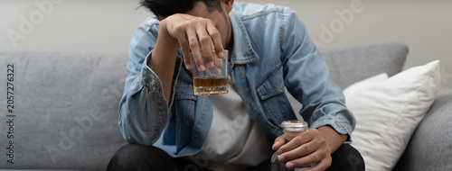 Schilderij op canvas Close-up of depressed young Asian man holding a glass of whiskey, suffering from alcoholism and mental health problems at home