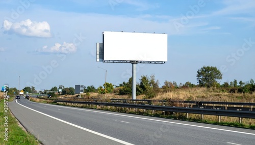 Blank white billboard on rural highway under blue sky.