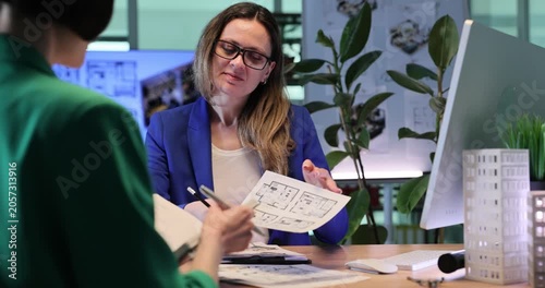 Designer shows technical sketches of apartments. Woman presents building designs and discusses construction possibilities with client. Slow motion