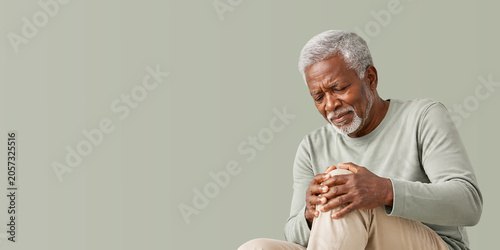Painful senior man holding knee. Older black man suffering from joint pain or arthritis. Health concept for geriatric care. banner format