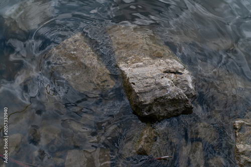 Natural rocky shoreline with gentle waves and sunlight reflecting on the water