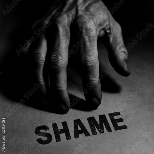 Weathered hand hovers over printed word shame evoking consequences and accountability in stark monochrome composition that conveys regret tension and introspection