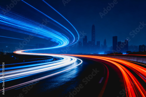 Long exposure shot showing light trails from moving vehicles on a curved urban highway at night, with a distant city skyline in the background.
