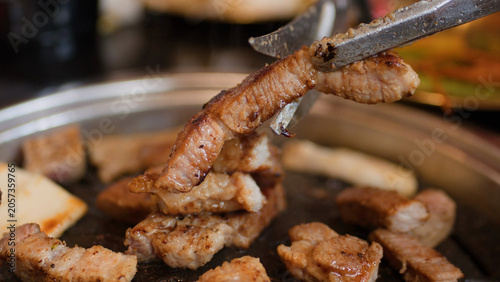 Cuadro en lienzo Close Up of Metal Tongs Lifting Grilled Pork Belly on BBQ Grill