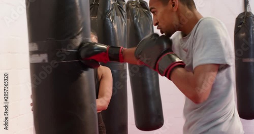 Female partner bracing bag while male boxer wearing gloves throwing punches, kicks in gym drill