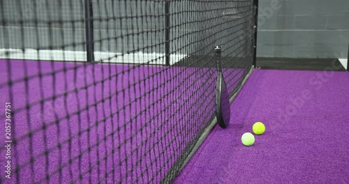Camera is panning right, revealing padel racket with balls on purple turf by black net